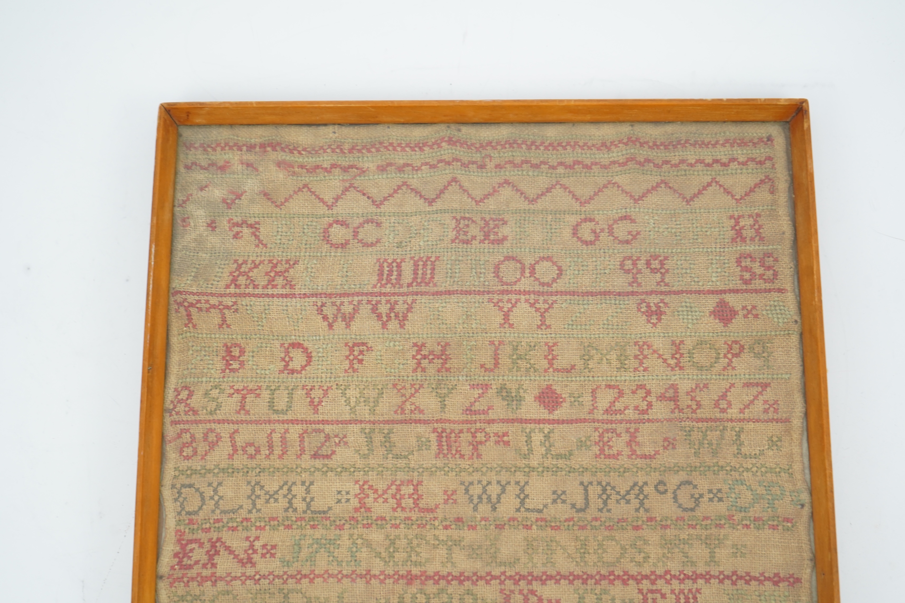 An alphabet cross stitch sampler with a figurative lower spot motif panel and commemorative dedication to John Lindsay, died Dec 16 1840, 27cm wide x 43.5 cm high. Condition - some light staining to linen, the blue and g